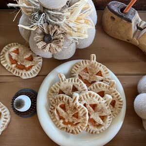 May include: A white plate with five pumpkin-shaped cookies with cinnamon and sugar on top. The cookies are arranged in a pile on the plate. The plate is on a wooden surface.