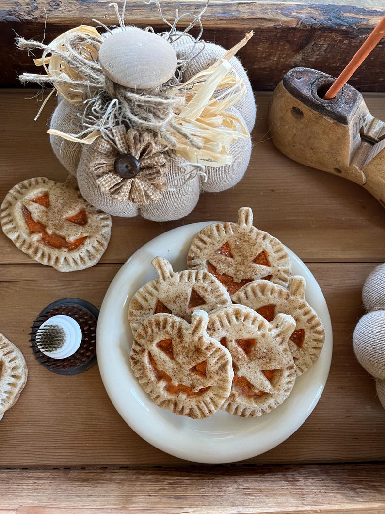 May include: A white plate with five pumpkin-shaped cookies with cinnamon and sugar on top. The cookies are arranged in a pile on the plate. The plate is on a wooden surface.