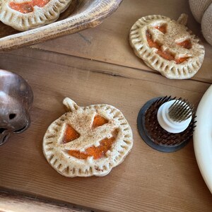 May include: Three pumpkin-shaped pie crusts with a jack-o'-lantern face design. The crusts are a light brown color with a cinnamon-sugar topping. The jack-o'-lantern faces are filled with a bright orange filling.