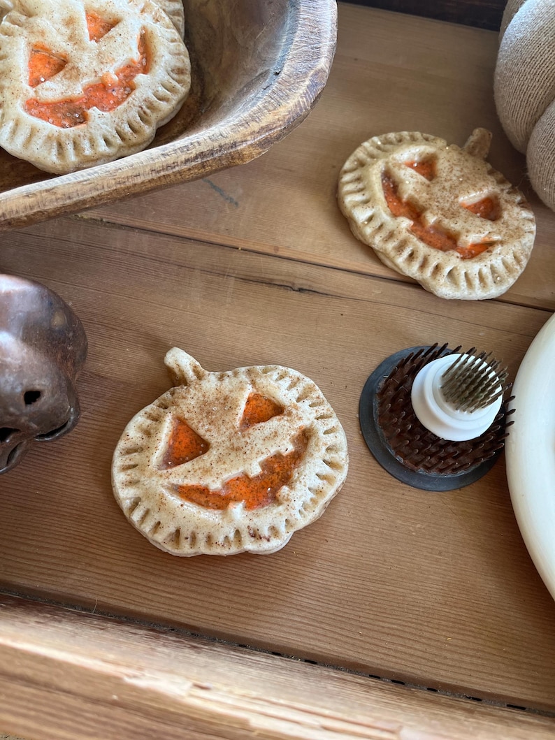 May include: Three pumpkin-shaped pie crusts with a jack-o'-lantern face design. The crusts are a light brown color with a cinnamon-sugar topping. The jack-o'-lantern faces are filled with a bright orange filling.