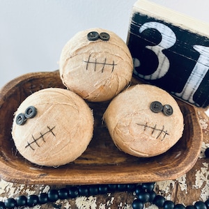 May include: Three spherical fabric-wrapped decorations in a tan color, each featuring two dark button eyes and a stitched mouth. The items are arranged in a brown wooden bowl next to a black and white wooden block displaying the number 31.
