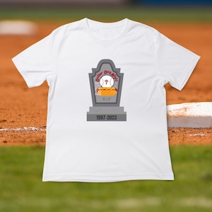 May include: White t-shirt with a gray tombstone graphic. The tombstone says "Dollar Dog Night" with a baseball and hot dog inside. The tombstone also says "R.I.P. 1997-2023".
