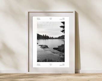 May include: Black and white photograph of a lake surrounded by trees. The lake is calm and the water is reflecting the sky. The trees are tall and thin, and they are growing on the shore of the lake.