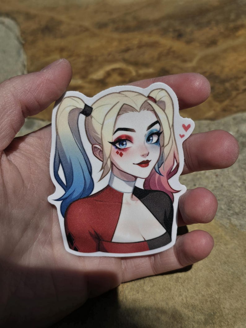 May include: A sticker featuring a cartoon illustration of Harley Quinn. She has blue and pink hair, red and black clothing, and a mischievous expression. She has red lipstick and blue eyeshadow. There are two small red hearts in the upper right corner of the sticker.