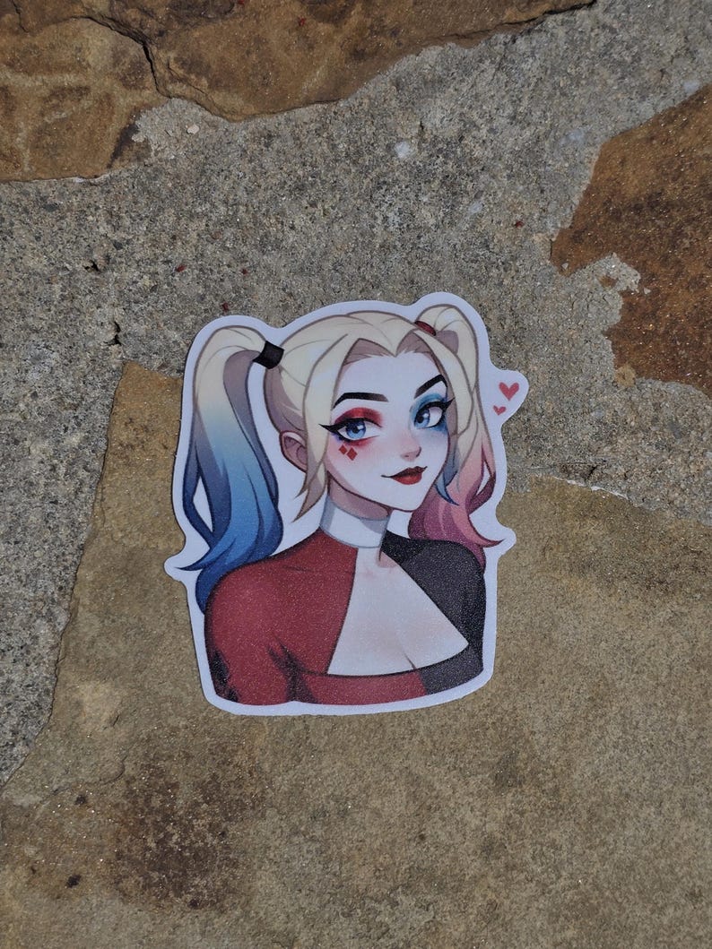 May include: A sticker featuring a cartoon illustration of Harley Quinn. She has blue and pink hair, red and black clothing, and a mischievous expression. She is wearing red lipstick and has hearts drawn on her cheeks.