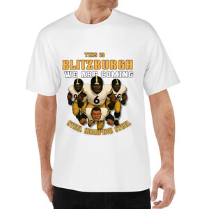 May include: White t-shirt featuring a graphic of football players in black and gold uniforms. The text "THIS IS BLITZBURGH WE ARE COMING" is printed above the players, with "STEEL SHARPENS STEEL" below.
