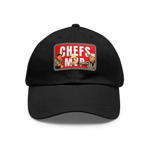 Op de afbeelding: Zwarte baseballpet met een gebogen klep. De pet heeft een rechthoekige patch met de woorden "CHEFS MVP" in het wit op een rode achtergrond. De patch bevat illustraties van koks.