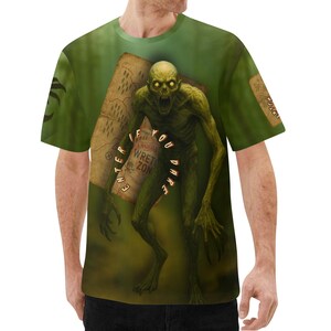 May include: Green t-shirt featuring a detailed illustration of a zombie-like creature with glowing yellow eyes and a map. The map has the text "ENTER IF YOU DARE WRETCH ZONE". The shirt has a green background.