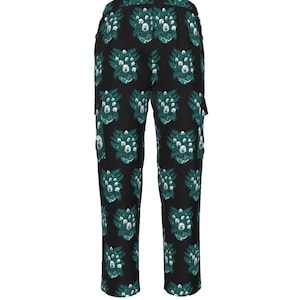 May include: Black trousers featuring a repeating pattern of green and white abstract designs. The trousers have a straight leg cut and a single pocket on the side. The fabric appears to be a lightweight material.