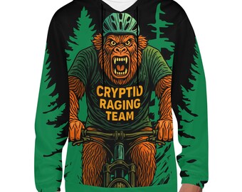 May include: A black hoodie with a green and black forest design. The front features a cartoon ape riding a bicycle, wearing a helmet and a green shirt with the text "CRYPTID RAGING TEAM".