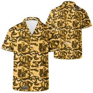 Puede incluir: Camisa amarilla y marrón de manga corta con un patrón repetido de caras y gafas. La camisa tiene cuello en V y el texto "THE CHIEF" en el cuello y "EST 1933" en la manga.
