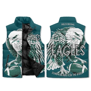 Peut inclure: Veste matelassée bleu sarcelle avec un aigle tenant un ballon de football. Le mot "EAGLES" est affiché, avec "PHILLY ORIGINAL" et "SUNDAYS ARE FOR THE BIRDS" imprimés sur la veste. La veste est de couleur sarcelle.
