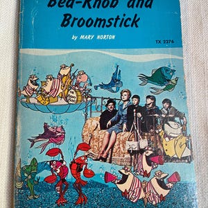 May include: A vintage paperback book titled Bed-Knob and Broomstick by Mary Norton, featuring a blue cover with an illustration of a woman and three children sitting on a bed surrounded by cartoon fish, lobsters, and a band called The Brainy Boys.
