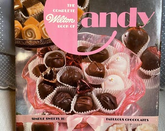 May include: The Complete Wilton Book of Candy features a large pink letter C on the cover, with the title text and images of assorted chocolates, truffles, and chocolate-covered strawberries in paper liners. A pink ribbon is at the bottom.