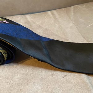 May include: A black and blue patterned tie with a yellow and pink design. The tie is rolled up and the pattern is visible on the rolled portion.