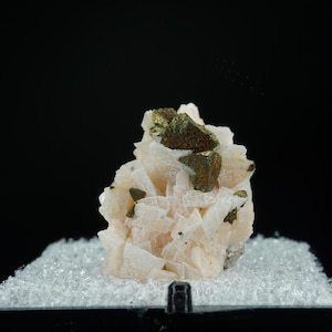 May include: A cluster of pale pink calcite crystals with embedded brassy pyrite crystals. The mineral specimen is displayed against a black background, showcasing its natural beauty and geological formation. The calcite crystals have a layered appearance.
