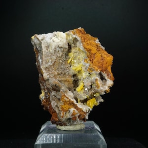 May include: A mineral specimen featuring a cluster of bright yellow, translucent crystals embedded within a rough, textured matrix of white quartz and earthy, rust-colored iron oxide deposits, mounted on a clear, square acrylic display base.