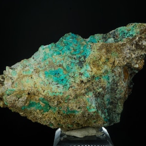 May include: A rough-hewn mineral specimen with a striking combination of colors. The rock features patches of vibrant turquoise and teal, contrasted by areas of tan and brown. The mineral is displayed against a black background.