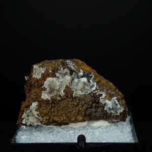 May include: A brown and white mineral specimen with white crystals on a black background.