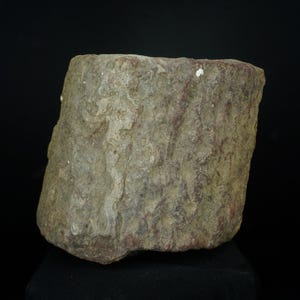 May include: A roughly rectangular stone vessel with a natural, weathered appearance. The stone is mainly grey with hints of red and brown, and has a textured surface. The object is set against a black background.