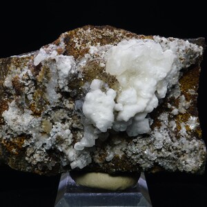 May include: A cluster of white calcite crystals on a brown matrix. The crystals are clustered together in a rounded shape, and they have a slightly translucent appearance. The matrix is rough and textured.