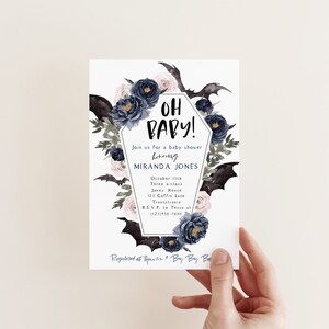 May include: A white baby shower invitation with a black and white coffin design. The coffin is decorated with black bats, pink and blue flowers, and the text "Oh Baby!"  The invitation includes the details for the baby shower, including the date, time, location, and RSVP information.