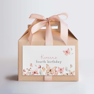 May include: A brown cardboard gift box with a pink ribbon and a white label that says "Kierra's fourth birthday". The label is decorated with pink and brown butterflies.
