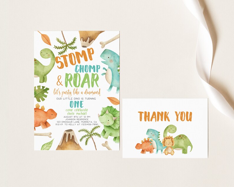 May include: A dinosaur-themed birthday party invitation with a green, orange, and blue color scheme. The invitation features a volcano, palm trees, and dinosaurs. The text on the invitation reads "Stomp, Chomp & Roar, let's party like a dinosaur! Our little dino is turning one. Come celebrate Oliver Michael, August 8th at 12 pm, Johnson Residence, 123 Dinosaur Lane, Murrieta, CA. RSVP to Kelly at 1231456-7890". A thank you card with a similar dinosaur theme is also included.