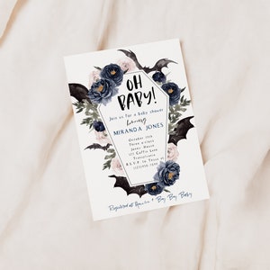 May include: A white baby shower invitation with a black coffin-shaped frame decorated with black bats, blue and pink flowers, and the text "Oh Baby!"  Join us for a baby shower honoring Miranda Jones.  October 11th, Three o'clock, Jones House, 123 Coffee Lane, Transylvania. RSVP to Tessa at (123) 456-7890.  Registered at Amazon + Buy Buy Baby.