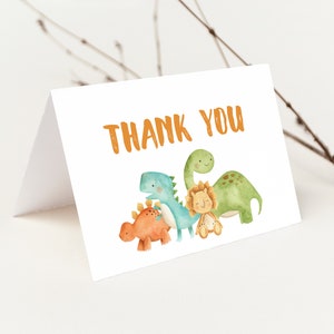 May include: Thank you card with a watercolor illustration of four dinosaurs. The dinosaurs are green, blue, orange, and yellow. The card has the text "Thank You" in orange.
