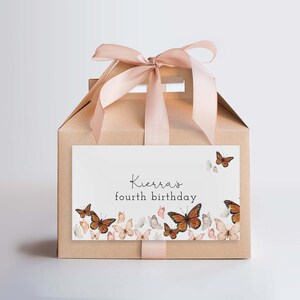 May include: A brown cardboard gift box with a pink ribbon and a white label that says "Kierra's fourth birthday". The label is decorated with butterflies.
