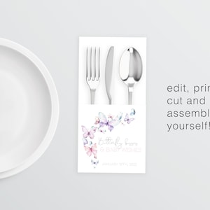 May include: A printable place card featuring a watercolor design of butterflies in shades of pink, purple, and blue. The text reads "Butterfly kisses & baby wishes" and "January 10th, 2022". The place card is designed to hold a fork, knife, and spoon.