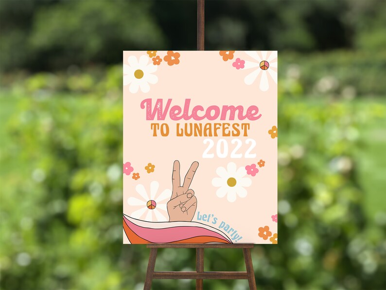 Peut inclure: Une pancarte d'accueil rose et blanche avec un signe de paix et des fleurs. La pancarte indique "Bienvenue &agrave; LunaFest 2022" et "Let's party !"