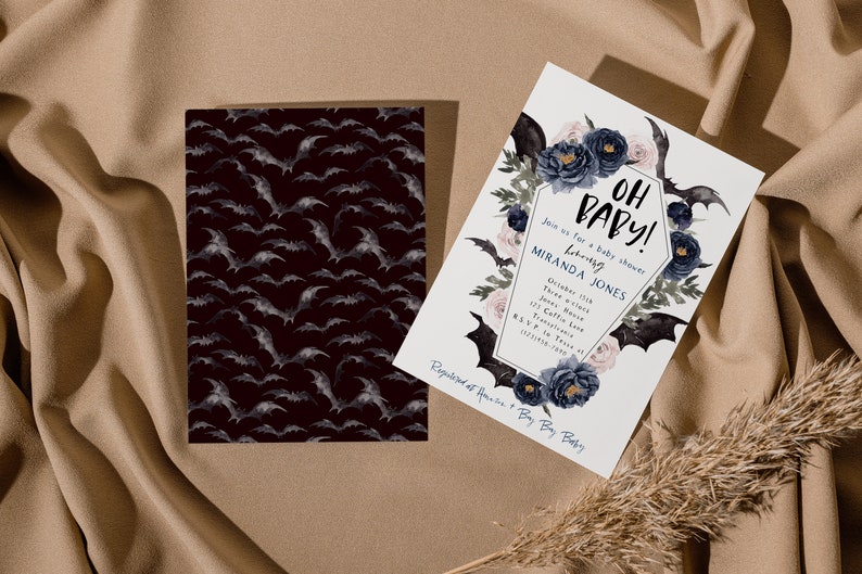 May include: A white baby shower invitation with a black coffin-shaped frame decorated with blue and pink flowers and bats. The text on the invitation reads "Oh Baby!" and includes the name "Miranda Jones".