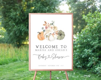 May include: A white sign with a brown frame welcomes guests to Marisa and Oscar's baby shower. The sign features a watercolor illustration of pumpkins and flowers in shades of orange, white, and green. The text "Welcome to Marisa and Oscar's Baby Shower" is written in a cursive font. The date of the shower is listed below: "Saturday, October 15th, 2023".