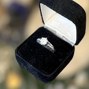 May include: A silver ring with a round diamond in a black velvet ring box.