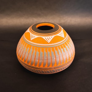 Może przedstawiać: Mały, pomarańczowy, ręcznie malowany wazon ceramiczny z geometrycznym wzorem. Wazon ma szeroki otwór i zaokrąglone ciało.