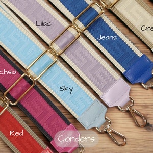 May include: A close-up of ten different coloured fabric straps with gold metal clasps. The straps are arranged in a row and labelled with the colours: Fuschia, Red, Sky, Lilac, Jeans, Cream, and Tan.