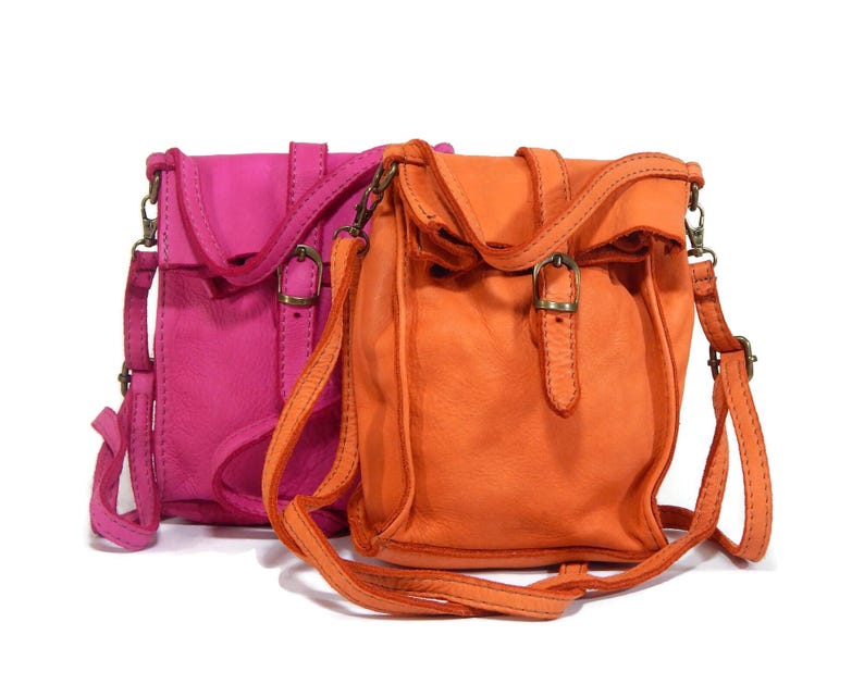 Puede incluir: Dos bolsos bandolera peque&ntilde;os de cuero, uno en rosa brillante y otro en naranja vibrante. Cada bolso cuenta con una solapa plegable con una correa vertical, un peque&ntilde;o cierre de hebilla met&aacute;lica y una correa fina ajustable con herrajes.