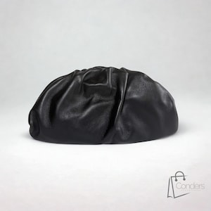 Peut inclure: Un sac pochette en cuir noir, de forme arrondie et plissée. Le sac présente un design froncé et une finition lisse et mate. Il est posé sur un fond blanc uni.