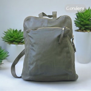 Puede incluir: Mochila de cuero verde oliva con un bolsillo frontal y cremalleras doradas. La mochila tiene un asa superior y correas ajustables. La palabra "Conders" está impresa en la esquina superior derecha.