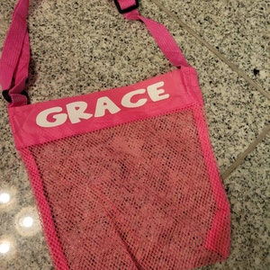 Peut inclure: Sac en filet rose avec une sangle réglable rose et le mot "GRACE" imprimé en blanc sur le devant.