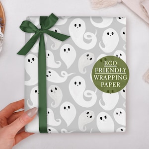 A hand holding a gift box with a ghost pattern and a green ribbon bow.