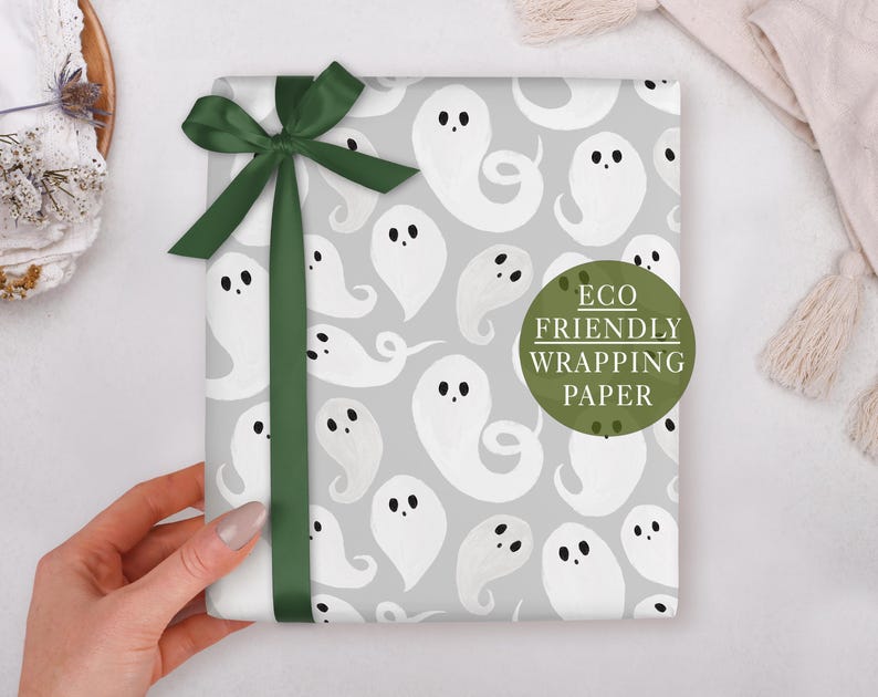 A hand holding a gift box with a ghost pattern and a green ribbon bow.
