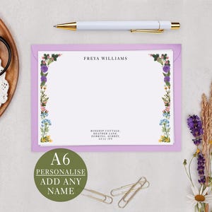 a personalized note card with a floral border, a pen, a pair of scissors, and some dried flowers.