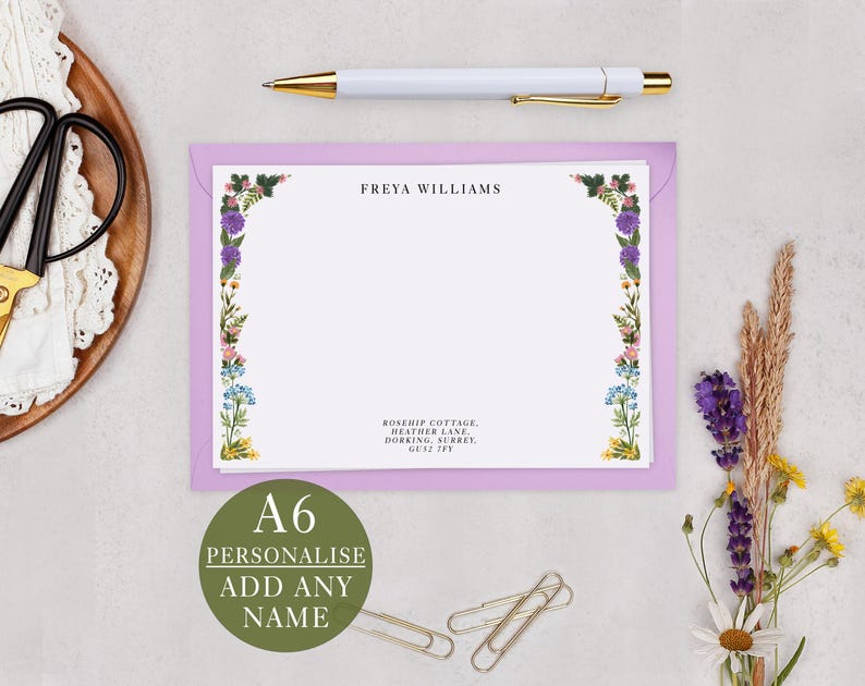 a personalized note card with a floral border, a pen, a pair of scissors, and some dried flowers.