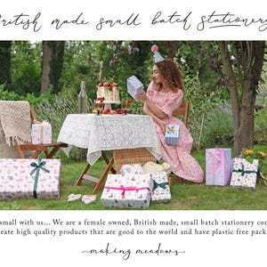 A woman in a pink dress is seated at a table with a cake and presents, surrounded by wrapped gifts and a wicker table.