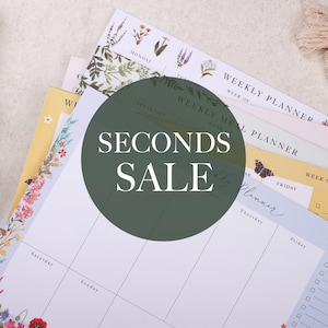 May include: A stack of floral patterned weekly planners with the text "SECONDS SALE" in a green circle.