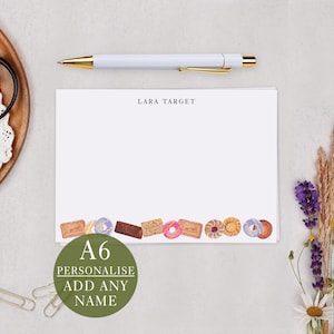 May include: A6 personalised stationery featuring a watercolour design of biscuits and doughnuts along the bottom edge. The text "LARA TARGET" is printed at the top. A white pen with gold detailing is above.