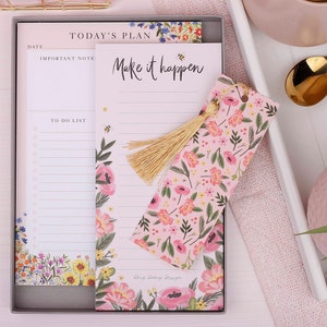 May include: A pink floral notepad with a matching bookmark. The notepad has a section for a date, an important note, and a to-do list. The bookmark has a tassel and the text "Make it happen".